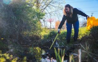 A woman is cleaning a stream with a yellow bucket.