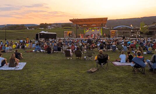 A crowd of people sitting on the grass at sunset.